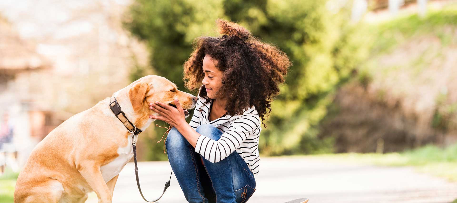 Girl with curly hair, caressing her pet dog on leash.